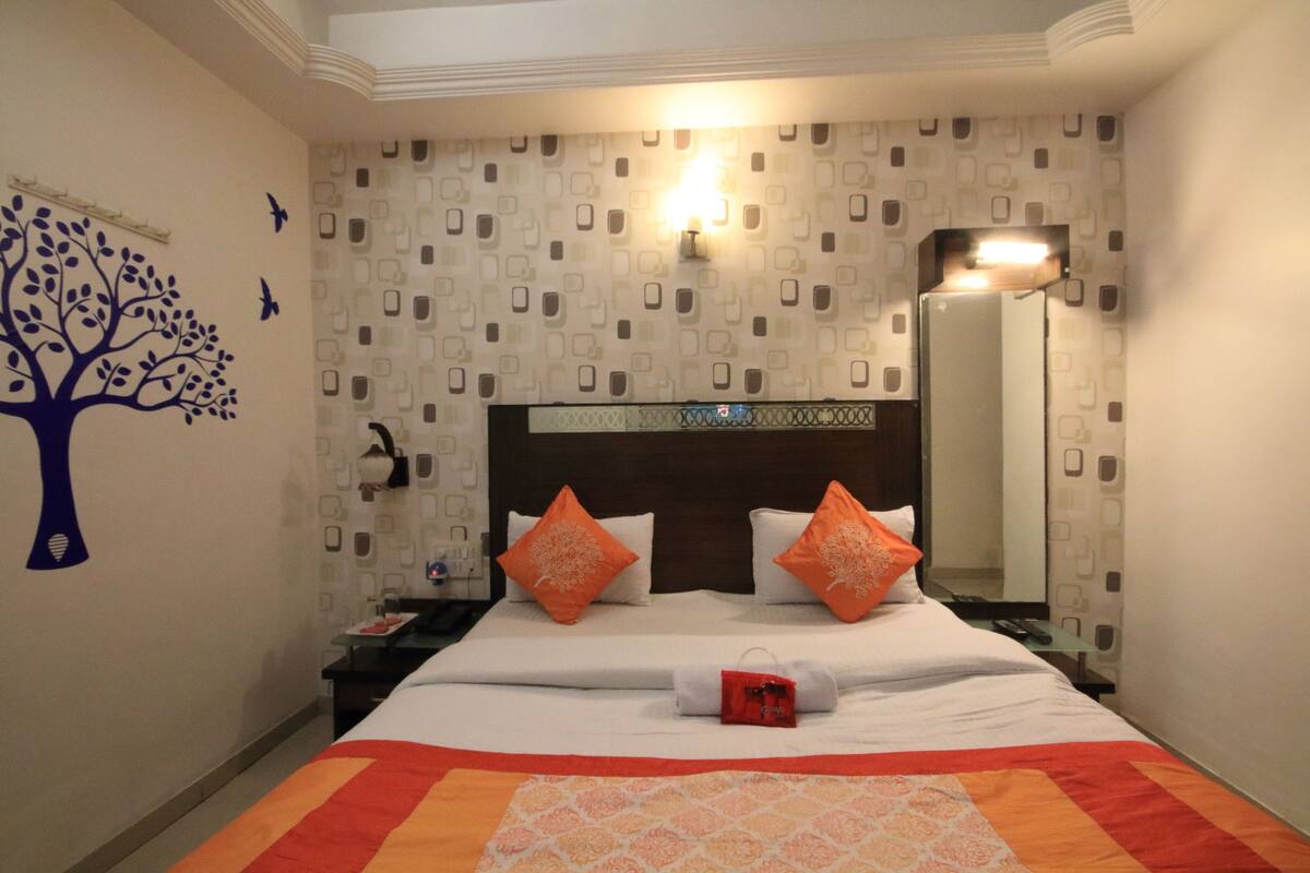 Een net opgemaakt bed met witte en oranje beddengoed, een sticker van een boom aan de muur en behang met een patroon.