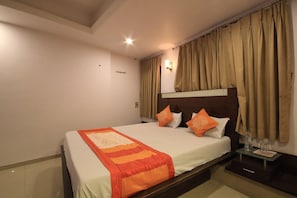 A neatly made bed with a striped blanket, a nightstand with a bottle and glasses, and a headboard with curtains.