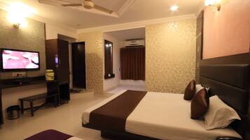 A hotel room with a bed, a TV, a desk, and a bathroom visible through an open door.