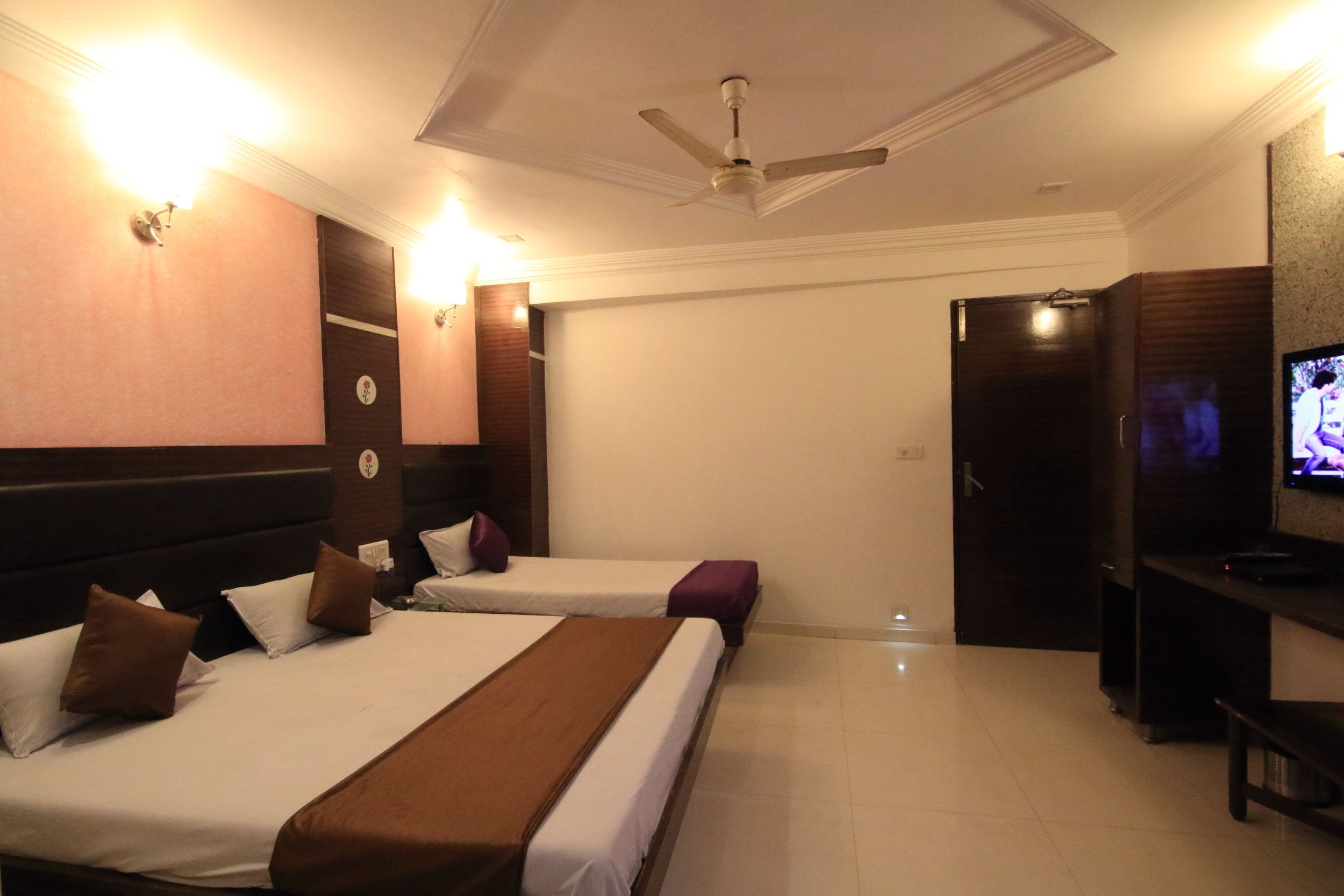 A hotel room with two beds, a TV, a ceiling fan, and a minibar.