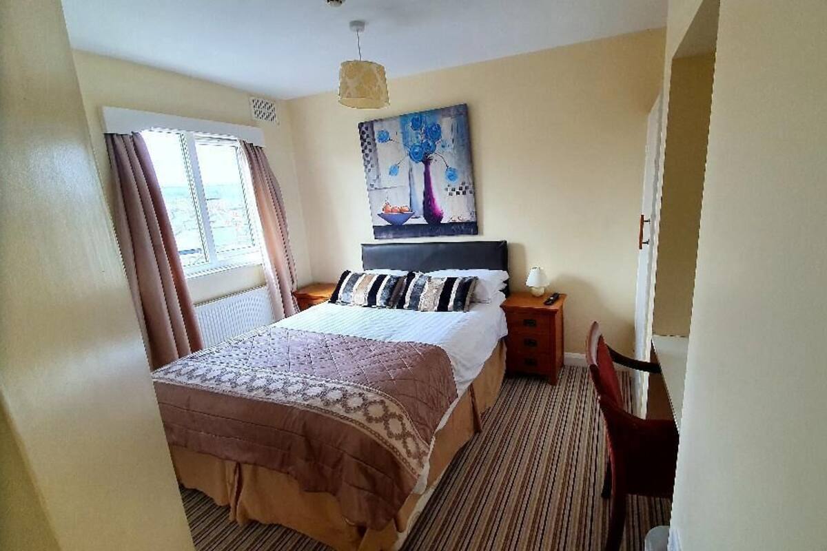 Een slaapkamer met een bed, een nachtkastje, een stoel, een schilderij aan de muur en een raam met gordijnen.
