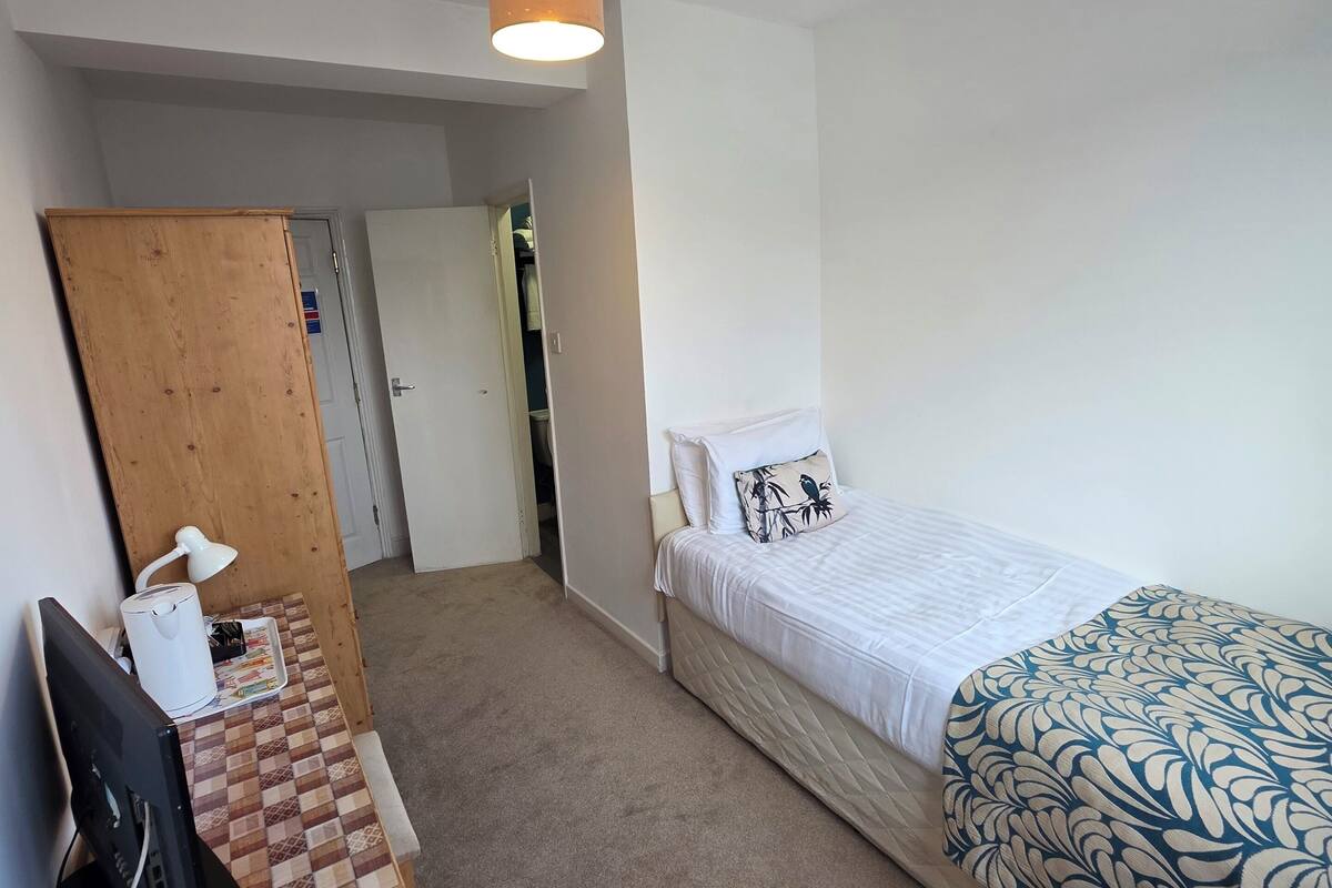 Een hotelkamer met een bed, een bureau met lamp, een kledingkast en een beveiligingscamera aan het plafond.