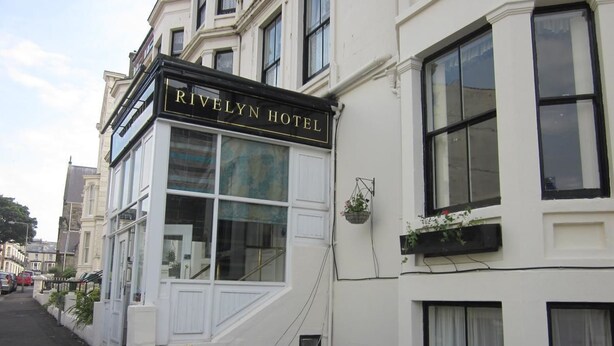 Un hôtel appelé Rivelyn Hotel, doté d’une façade classique, de grandes fenêtres et d’une enseigne bien visible.