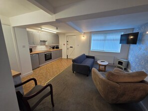 A compact living space with a kitchenette, a sofa, a small table, and a TV mounted on the wall.