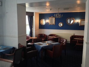 A dining area with tables and chairs, a chandelier, and decorative mirrors on the wall.
