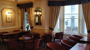 Une chambre d’hôtel dotée d’un coin repas avec des tables et des chaises en bois, un lustre et de grandes fenêtres avec des rideaux.