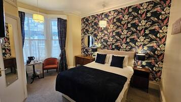 A bedroom with a large bed, a nightstand, a dresser, a chair, and a window with curtains.