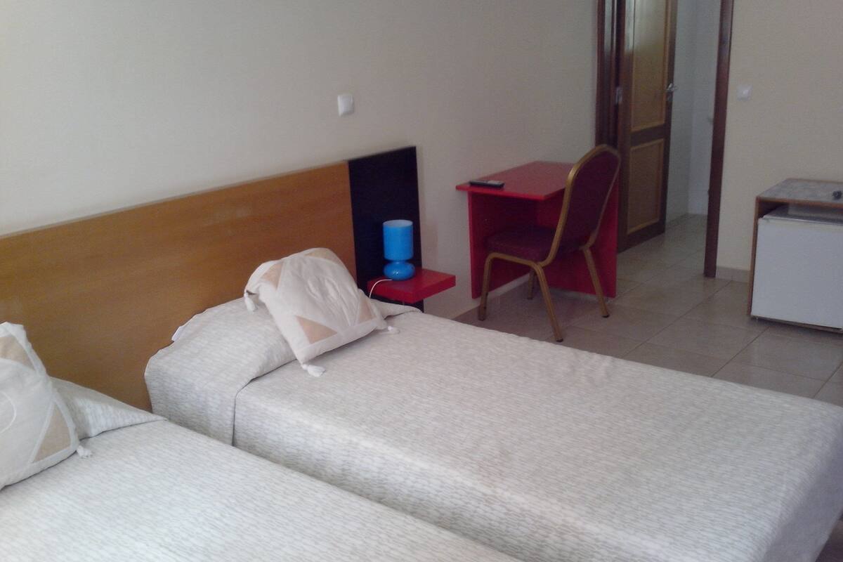 Una habitación de hotel con dos camas individuales, un escritorio, una silla y un armario pequeño.