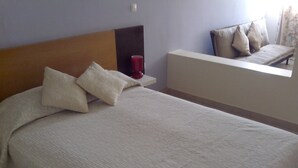 A neatly made bed with pillows, a bedside table with a red object, and a sofa with cushions. - Tarrafal Residence (Tarrafal)