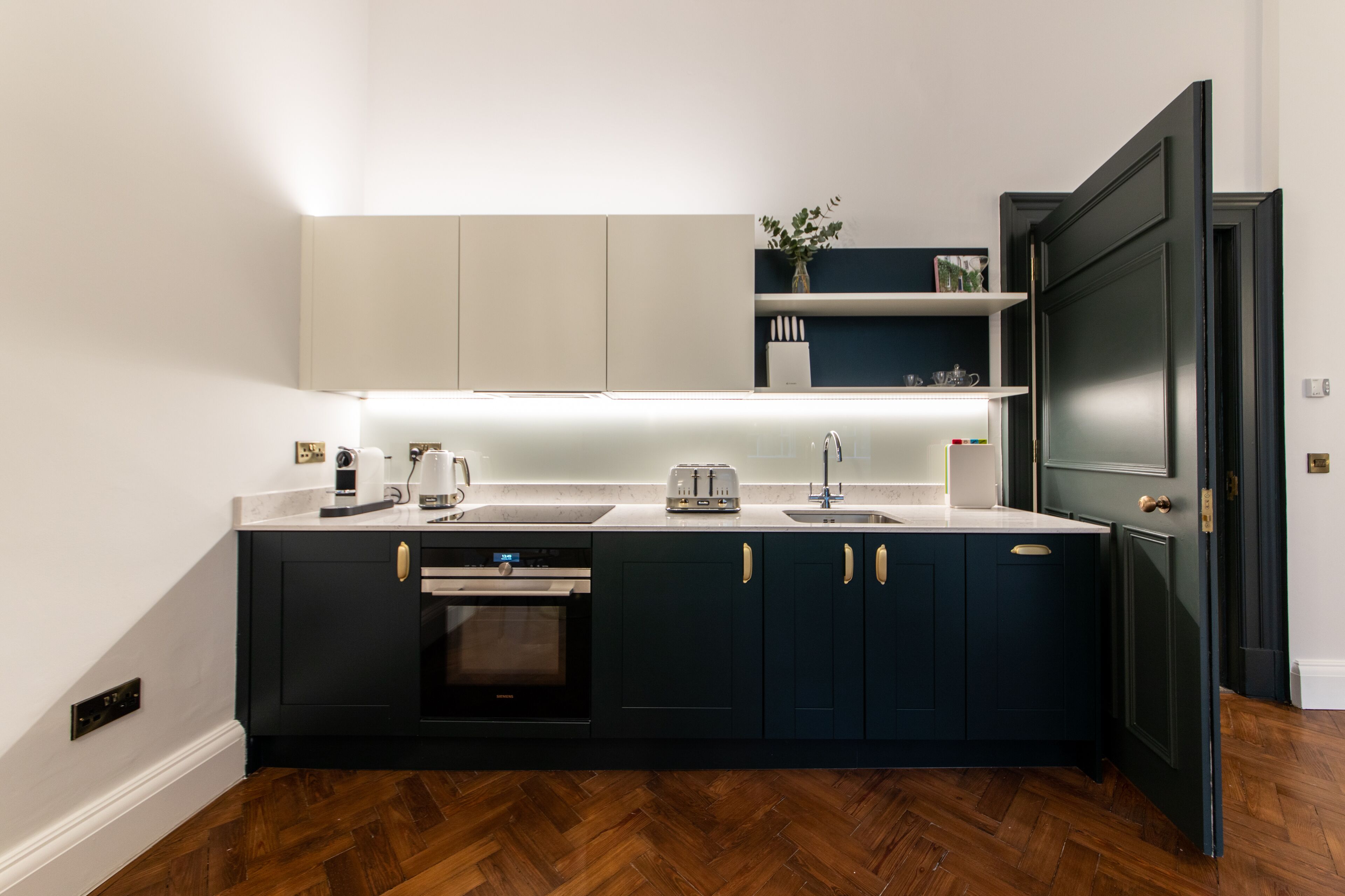 A compact kitchen with dark cabinetry, a built-in oven, a sink, and a countertop with a toaster and kettle.
