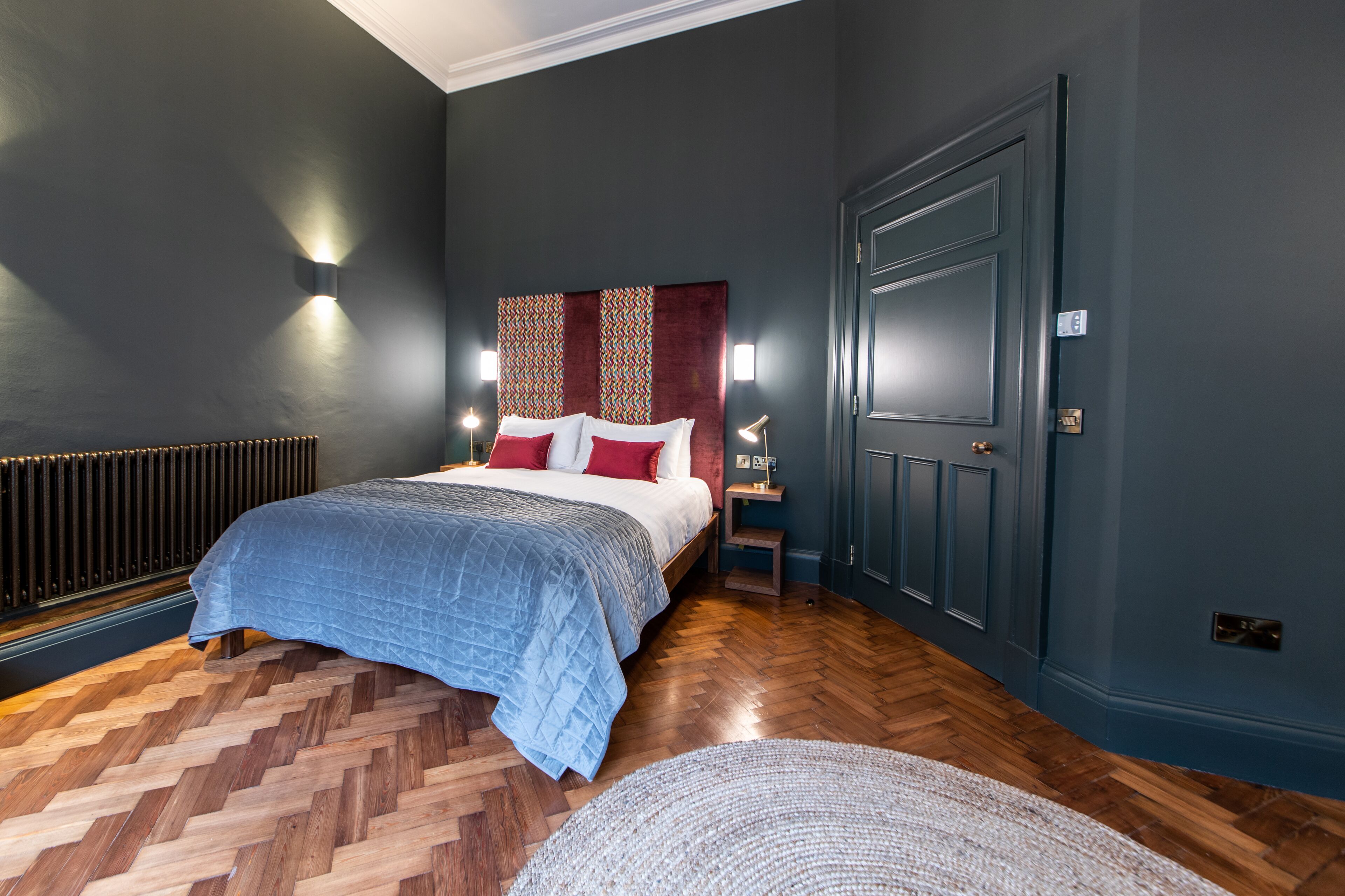 A bedroom with a bed, a radiator, a nightstand, and a door.