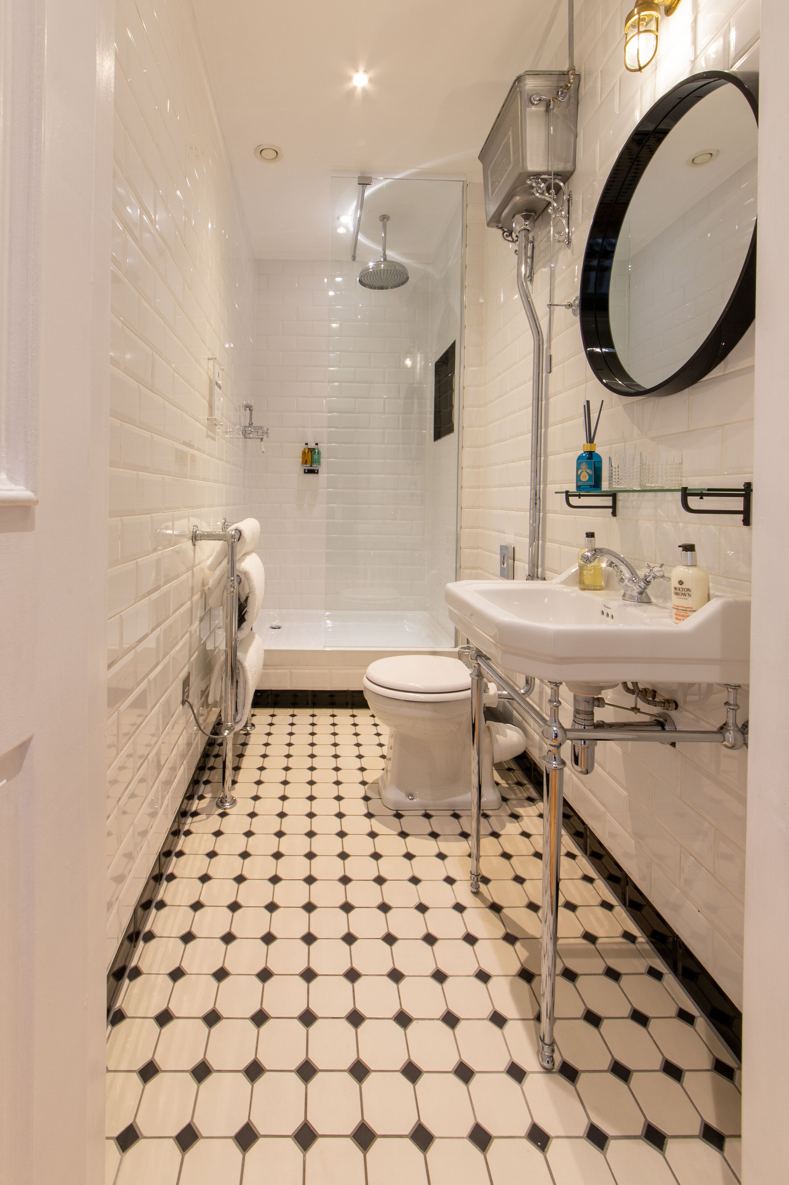 A bathroom with a white tiled floor, a white toilet, a white sink, a mirror, and a shower.