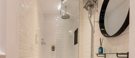 A bathroom with a white tiled floor, a white toilet, a white sink, a mirror, and a shower.