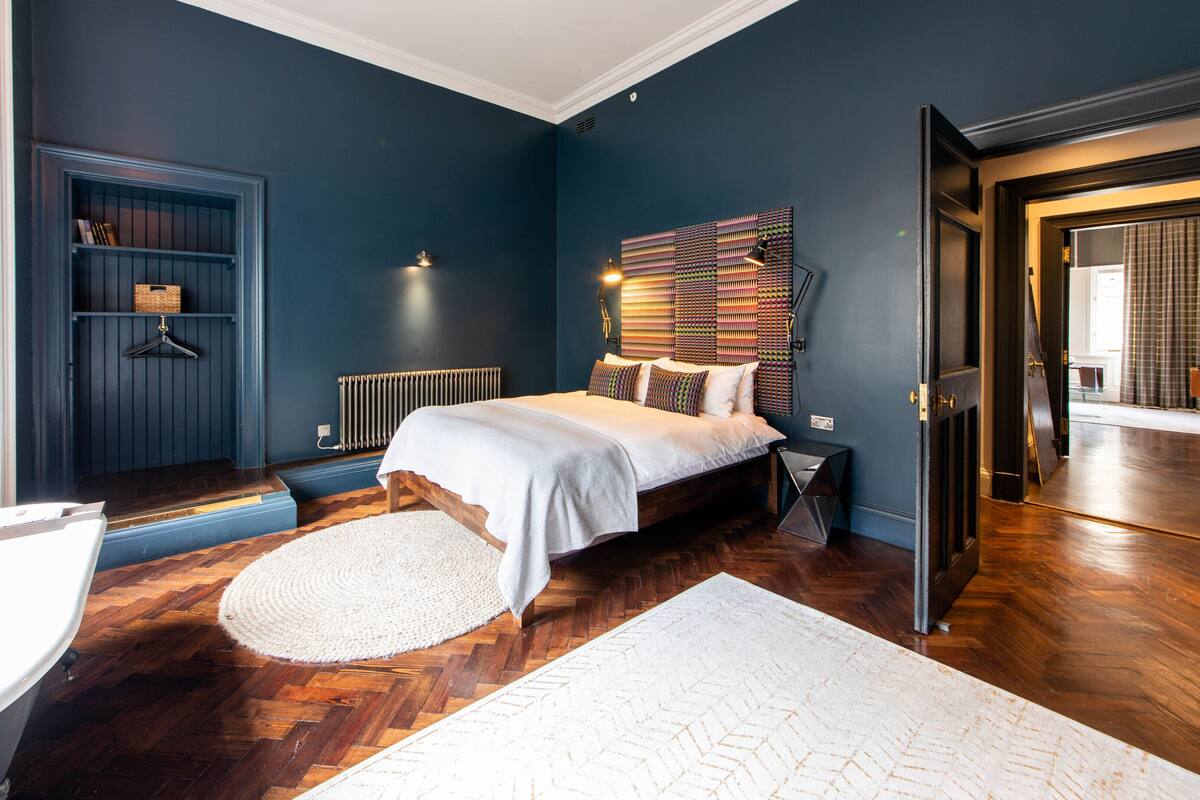 Une chambre avec un lit, un radiateur, un tapis rond blanc et un plancher en bois.