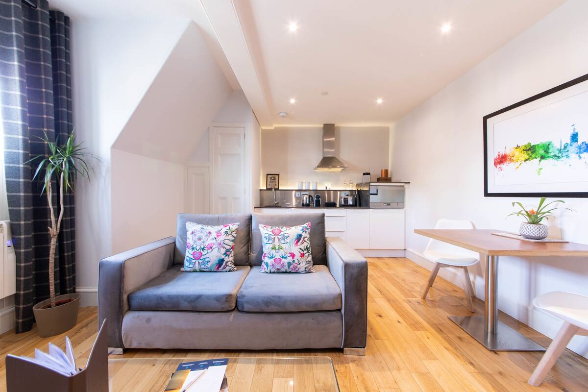 Un salon moderne avec un canapé gris, une table basse en bois et un coin repas comprenant une table et des chaises blanches.