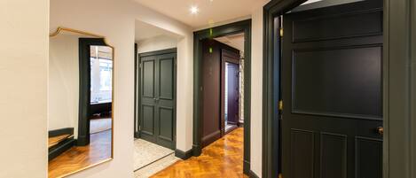 A hallway with wooden flooring, dark doors, and a mirror on the left wall.