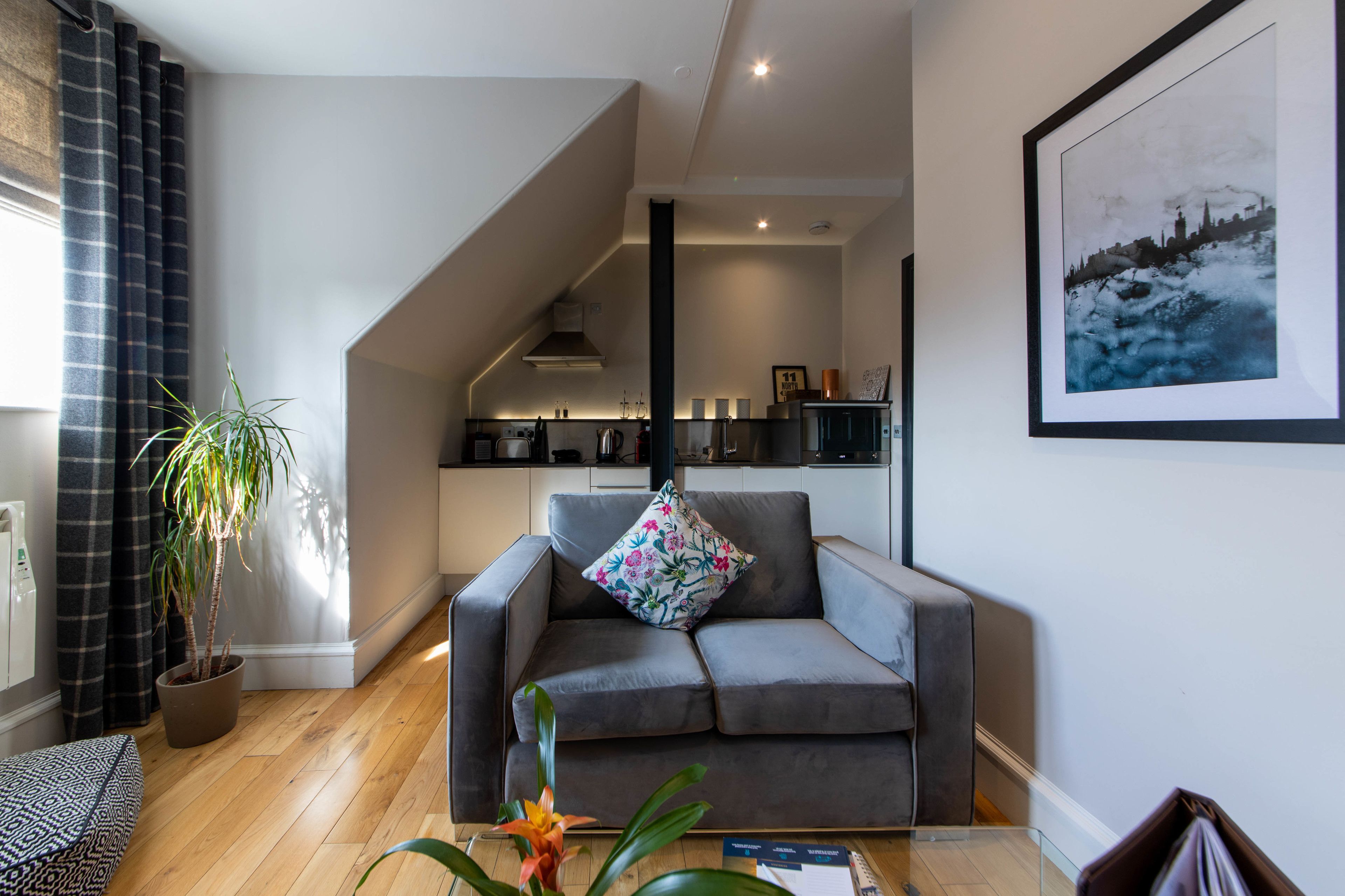 Una sala de estar moderna con un sofá gris, una planta en maceta y un cuadro con una vista urbana en la pared.