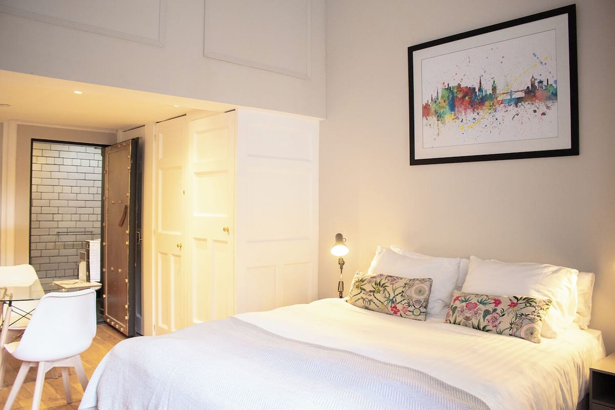 Une chambre d’hôtel avec un lit, un bureau et une chaise. Une porte donne accès à une autre pièce.