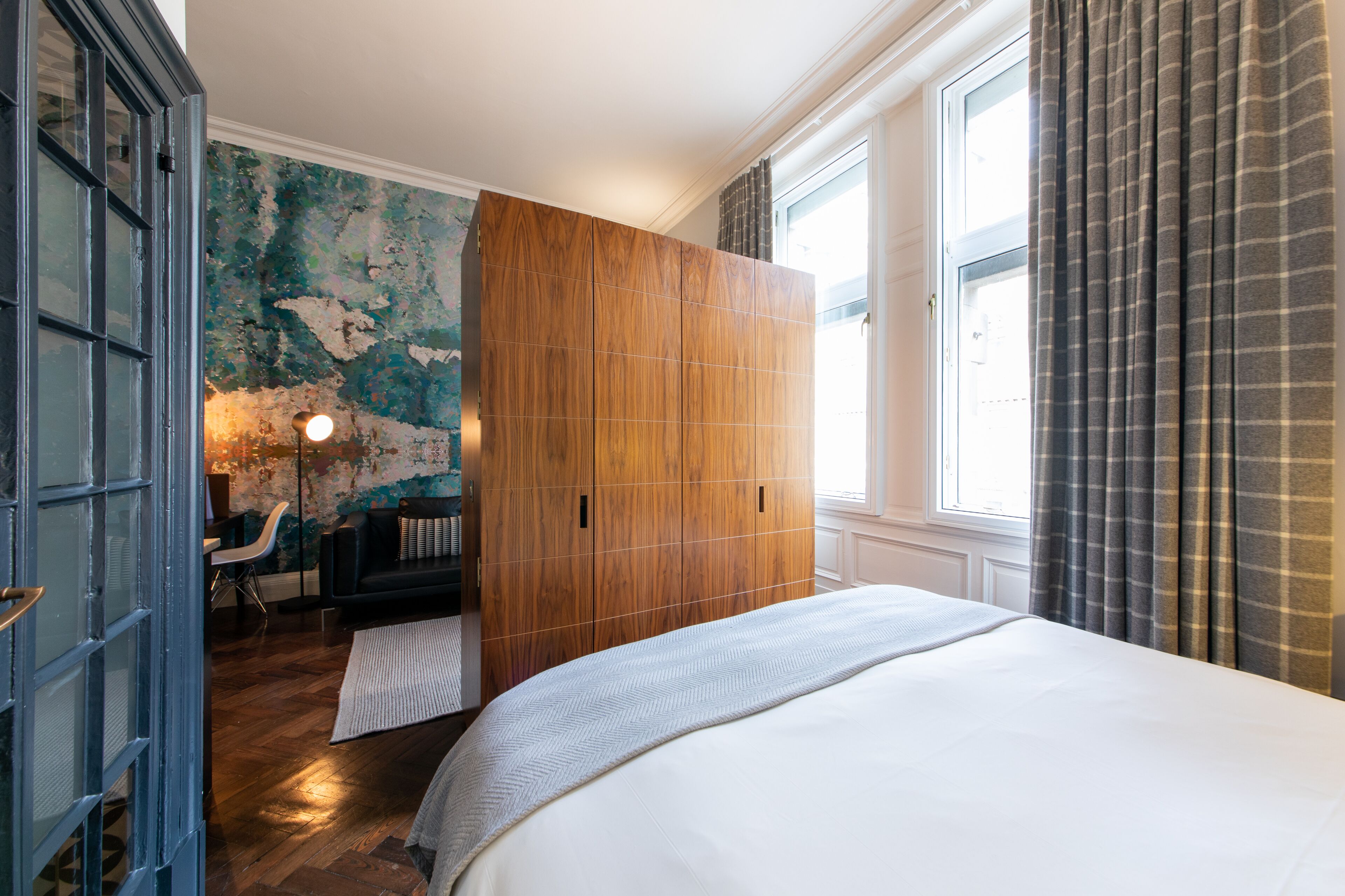 A hotel room with a large bed, a wooden wardrobe, a desk with a chair, and a wall with a distressed paint finish.