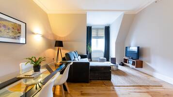 Een moderne woonkamer met een bank, een glazen eettafel, een televisie en een potplant.