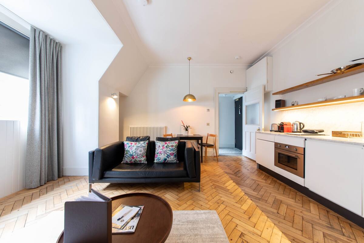 Un salon moderne avec un canapé noir, une table basse et un coin repas comprenant une table et des chaises.
