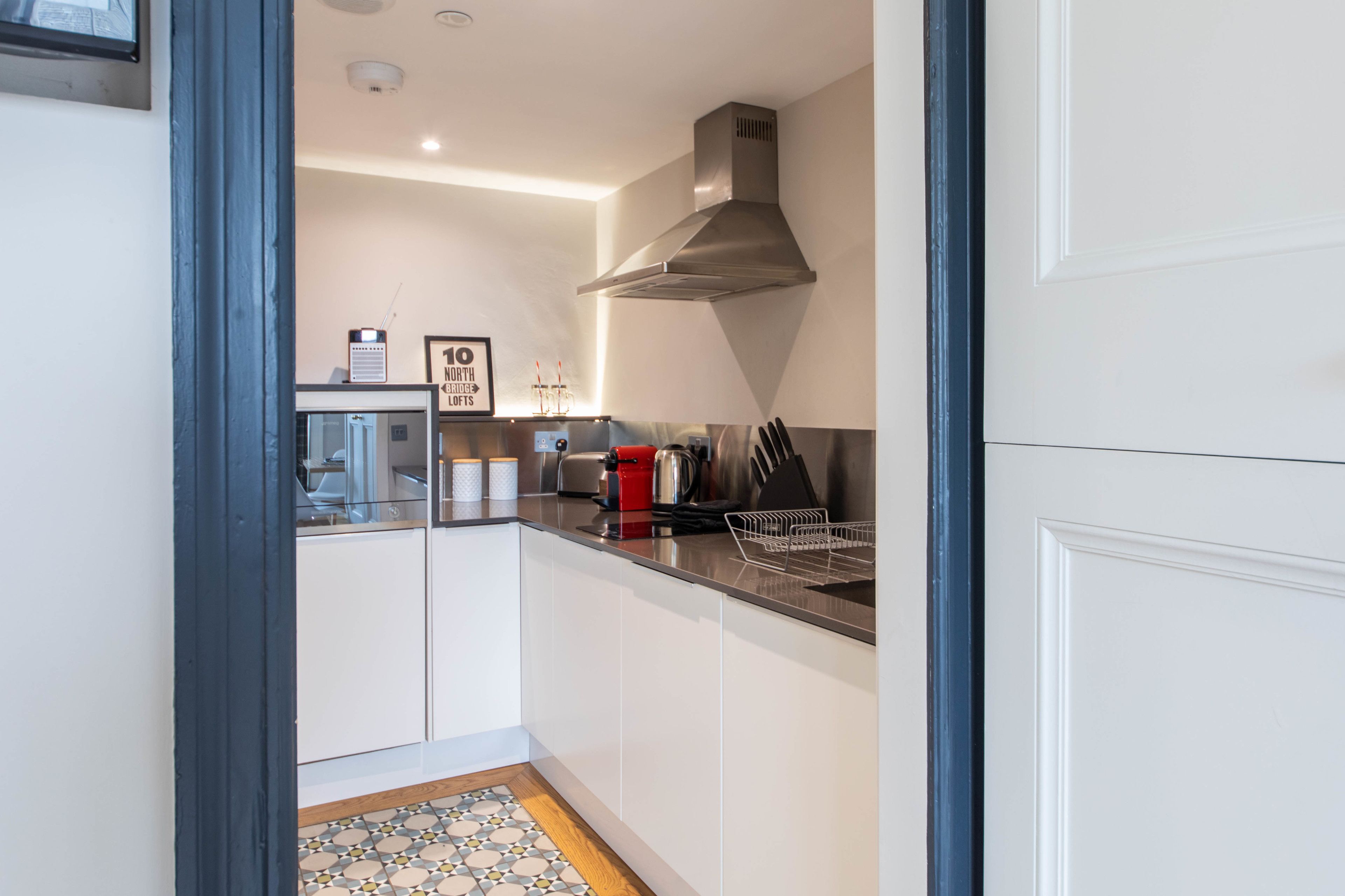 A compact kitchen with white cabinets, a stainless steel range hood, and a tiled backsplash.