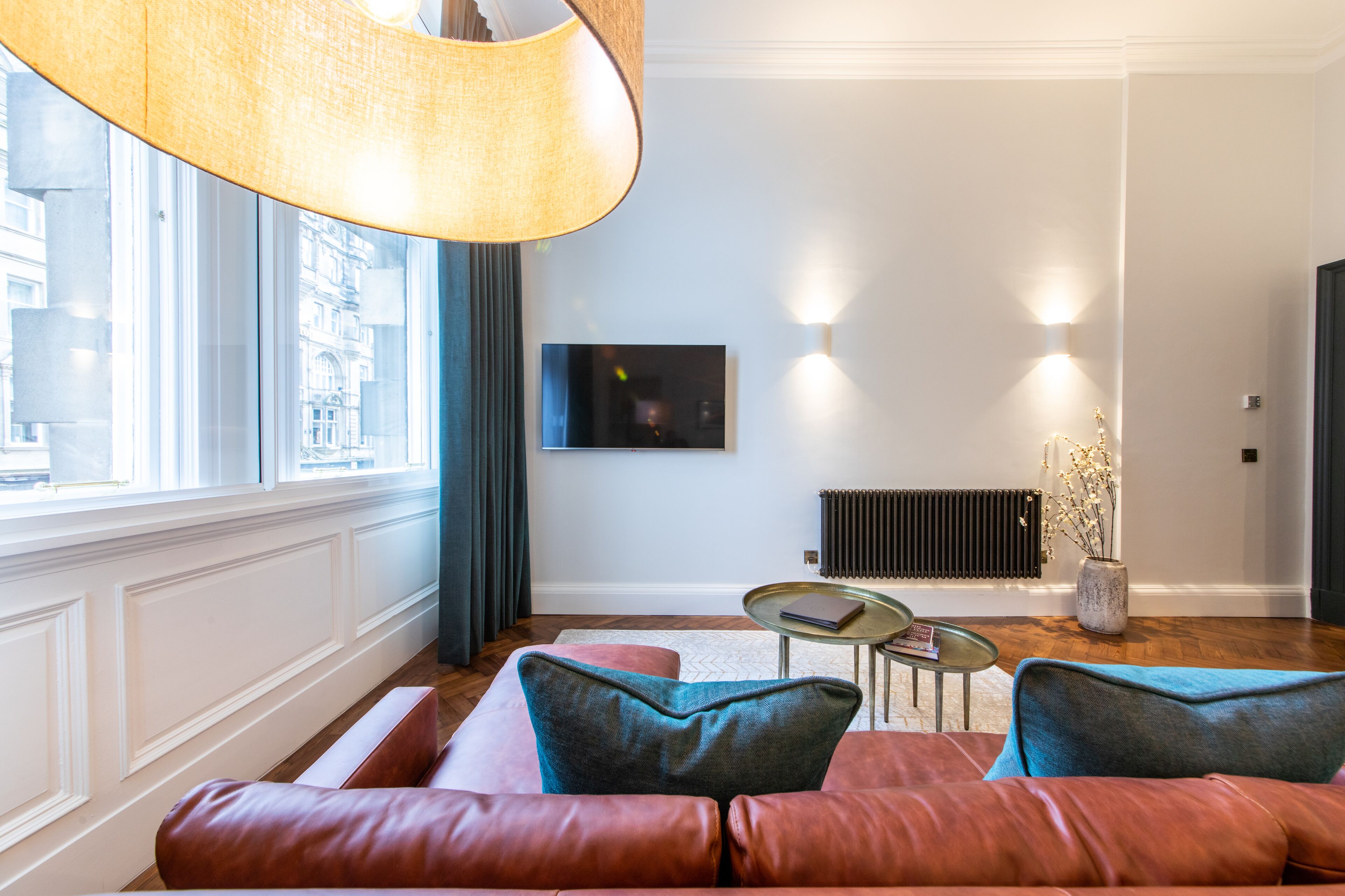 Een moderne woonkamer met een leren bank, een ronde salontafel en een groot raam met gordijnen.