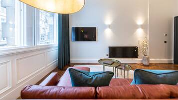 Een moderne woonkamer met een leren bank, een ronde salontafel en een groot raam met gordijnen.