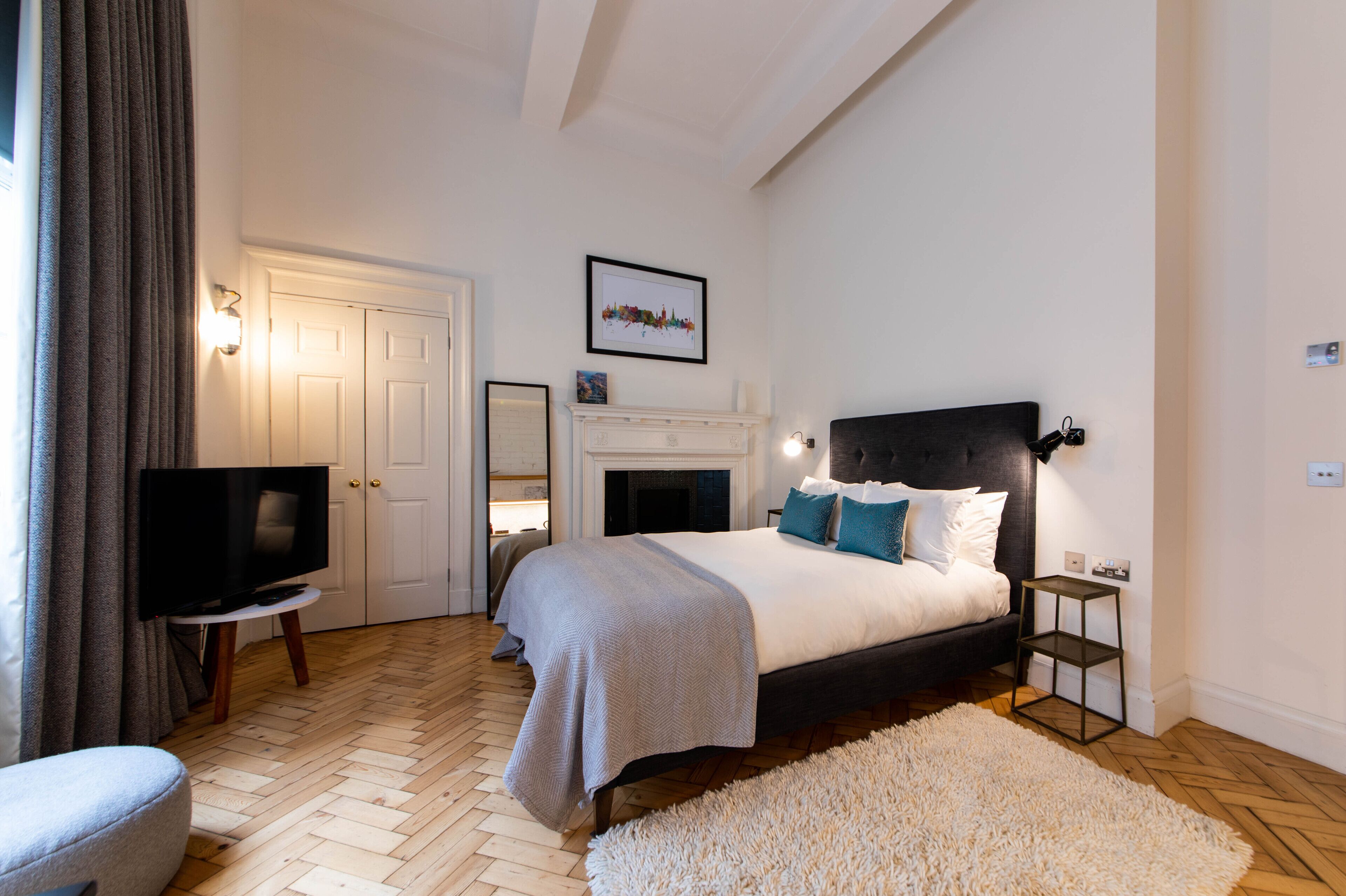 A bedroom with a bed, a television, a fireplace, and a white wall with a framed picture.