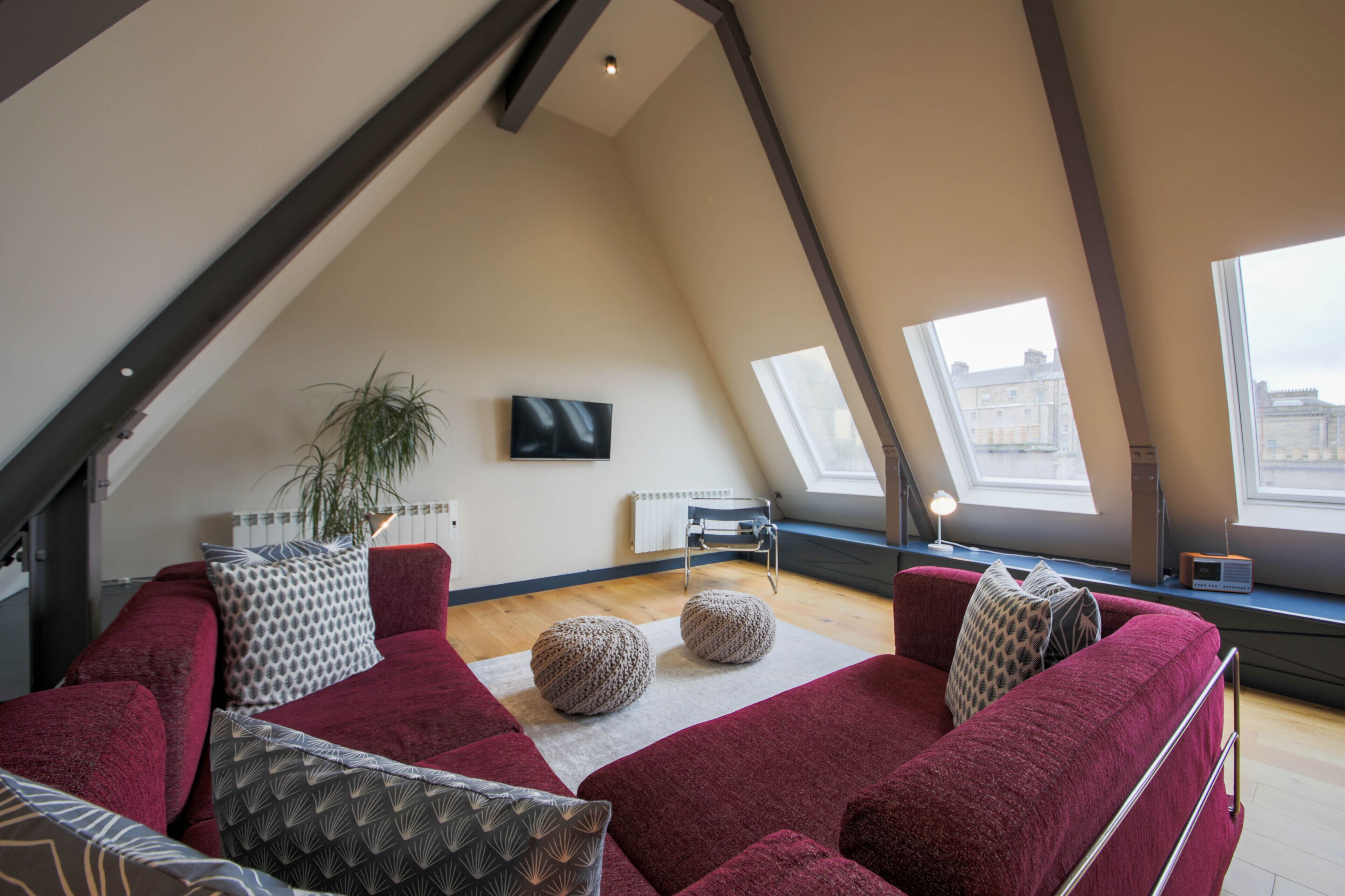 A cozy loft-style living room with a red sofa set, a potted plant, and a flat-screen TV mounted on the wall.