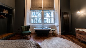 Une pièce avec une grande fenêtre, une baignoire, une chaise et une table de chevet.