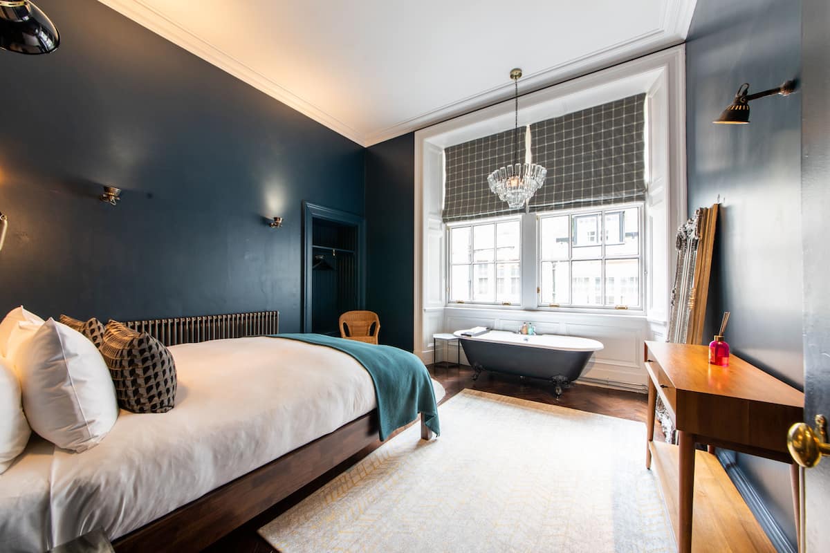 Une chambre avec un grand lit, une baignoire et une fenêtre donnant sur des immeubles.