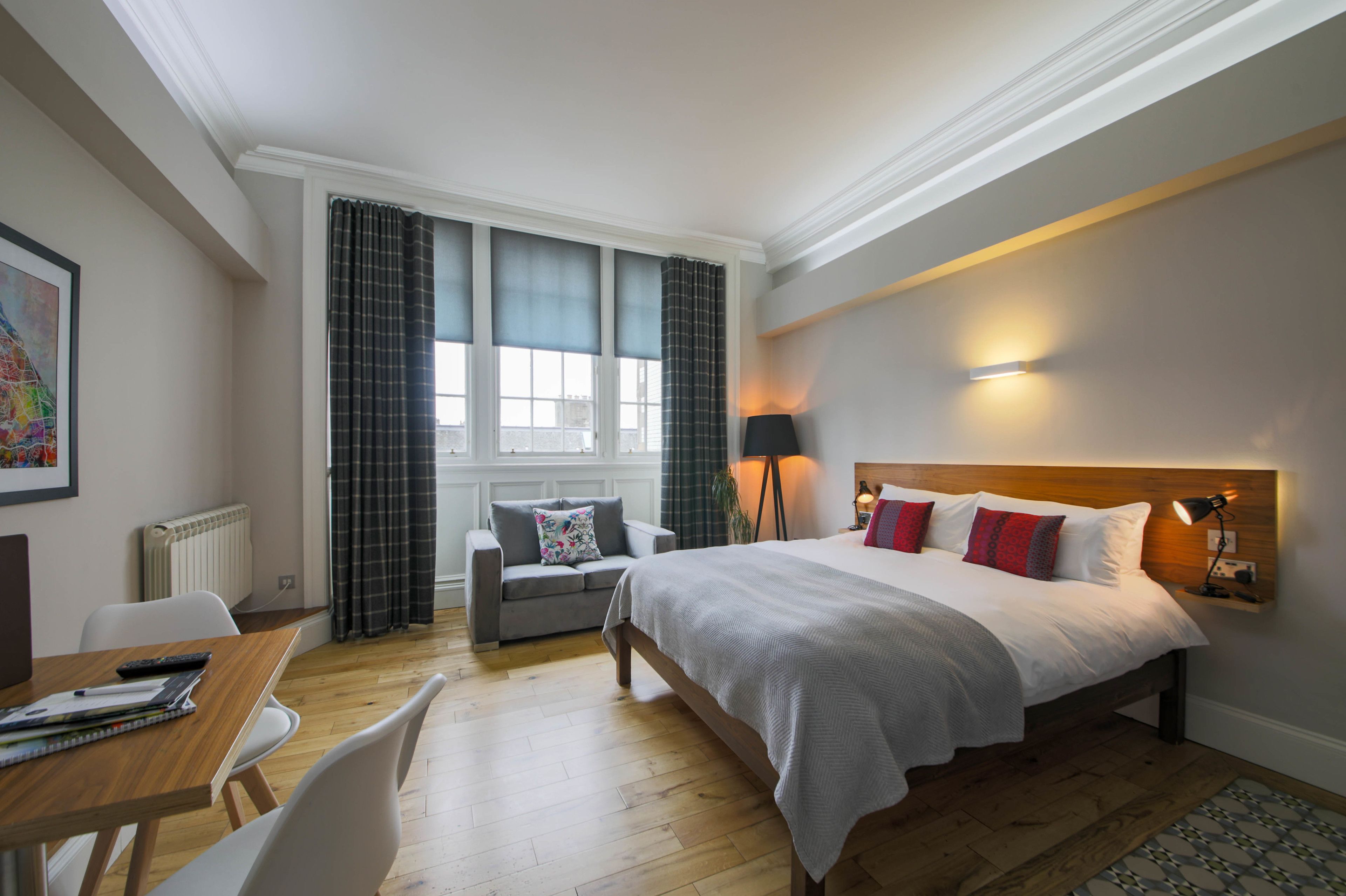 Una habitación de hotel moderna con una cama grande, un escritorio con silla, un sofá y una ventana con cortinas.