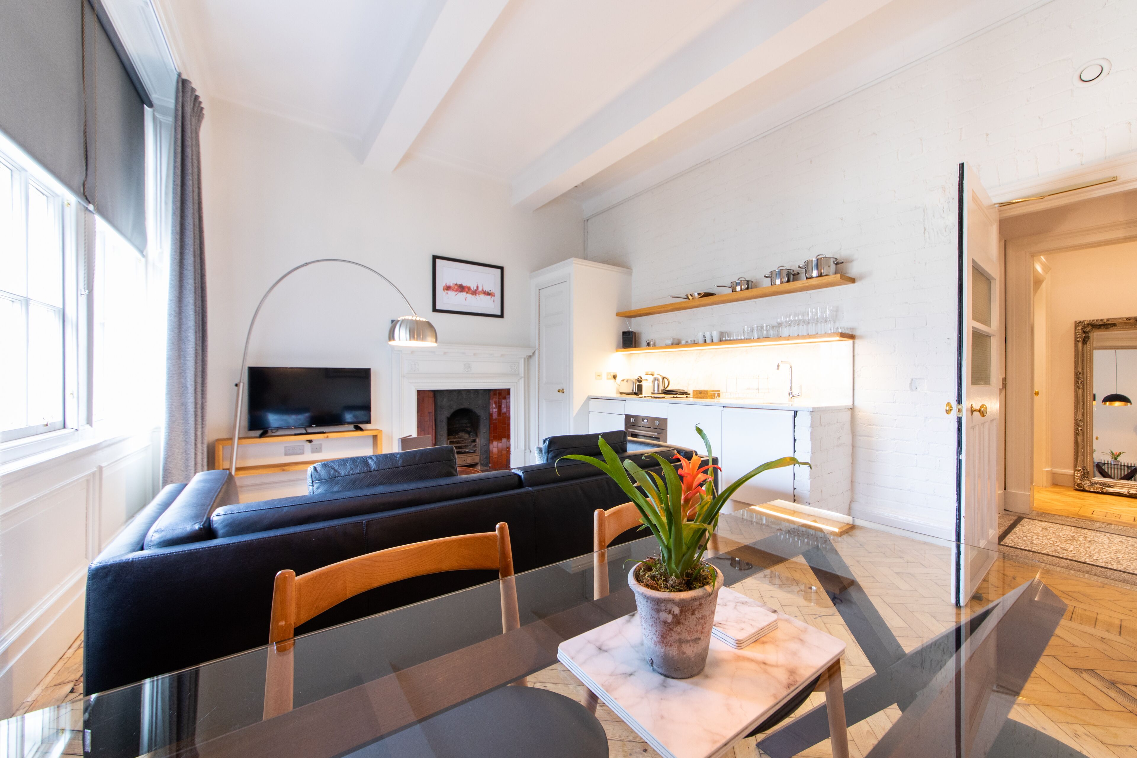 A modern living room with a black sectional sofa, a glass dining table, and a potted plant.