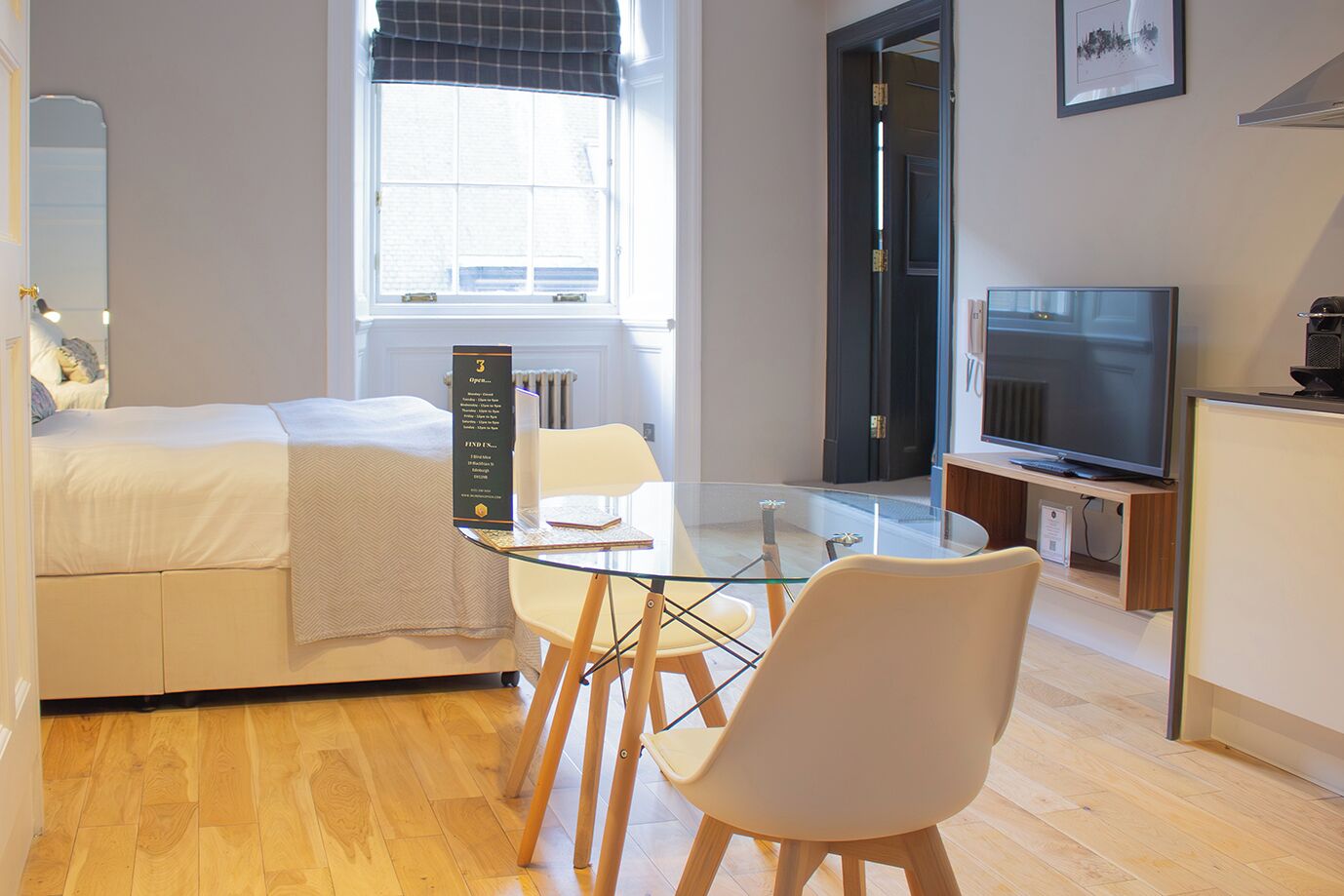 Moderni hotellihuone, jossa on sänky, lasinen ruokapöytä, televisio ja näkymä kaupunkiin.