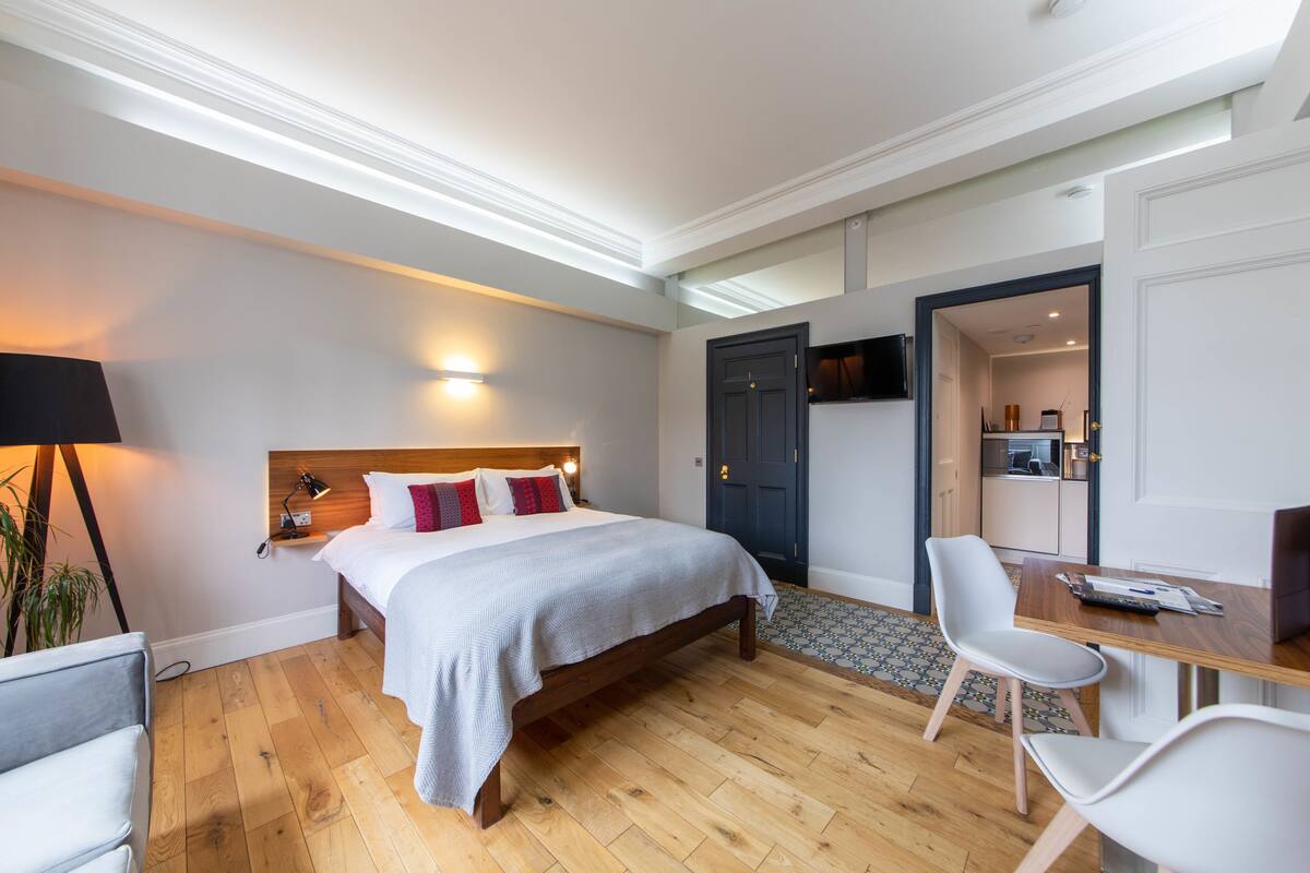 Une chambre d’hôtel comprenant un lit, une table de chevet, une lampe et donnant sur la cuisine.