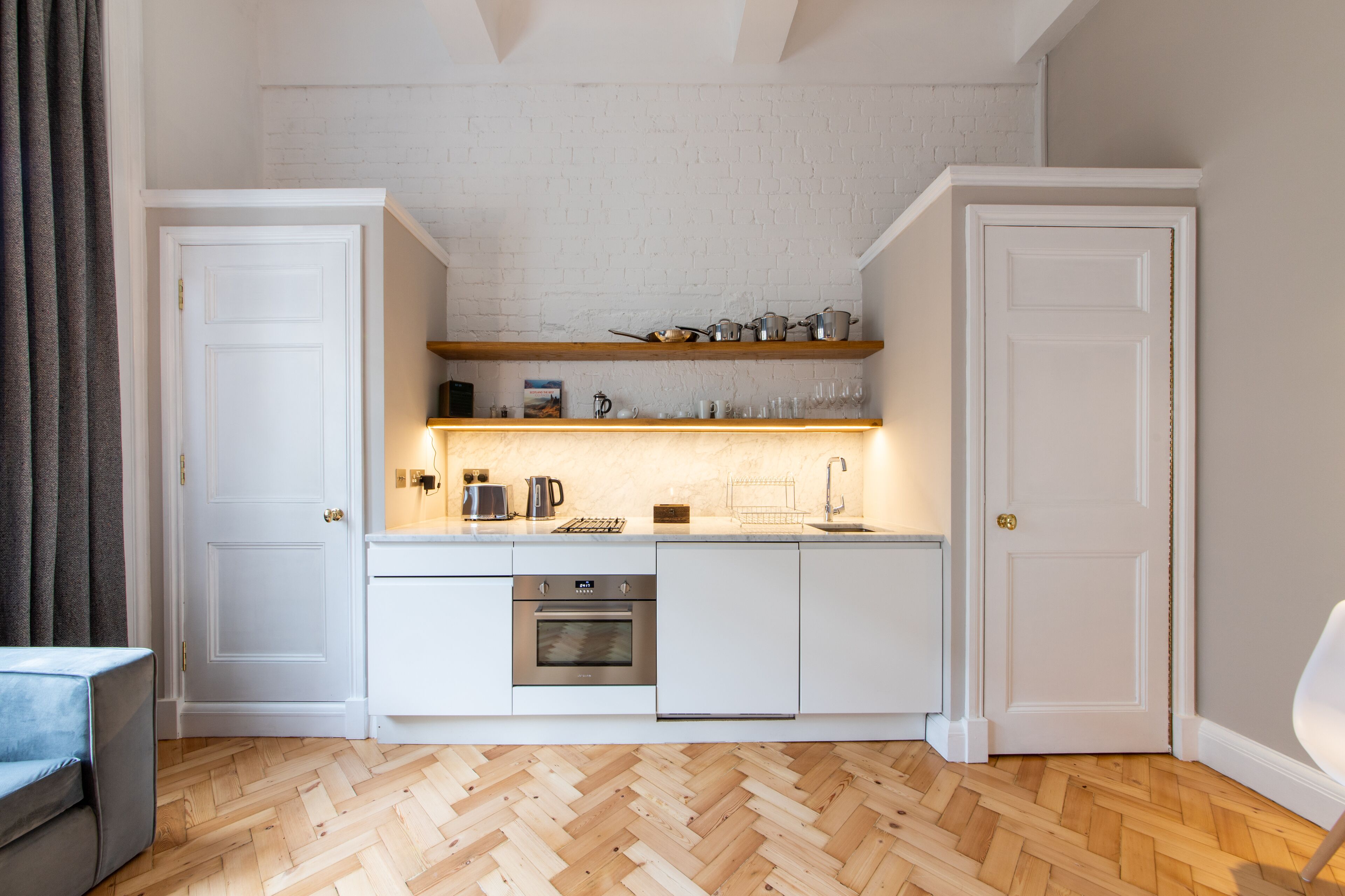 Een compacte keuken met witte kastjes, een ingebouwde oven en een houten visgraatvloer.