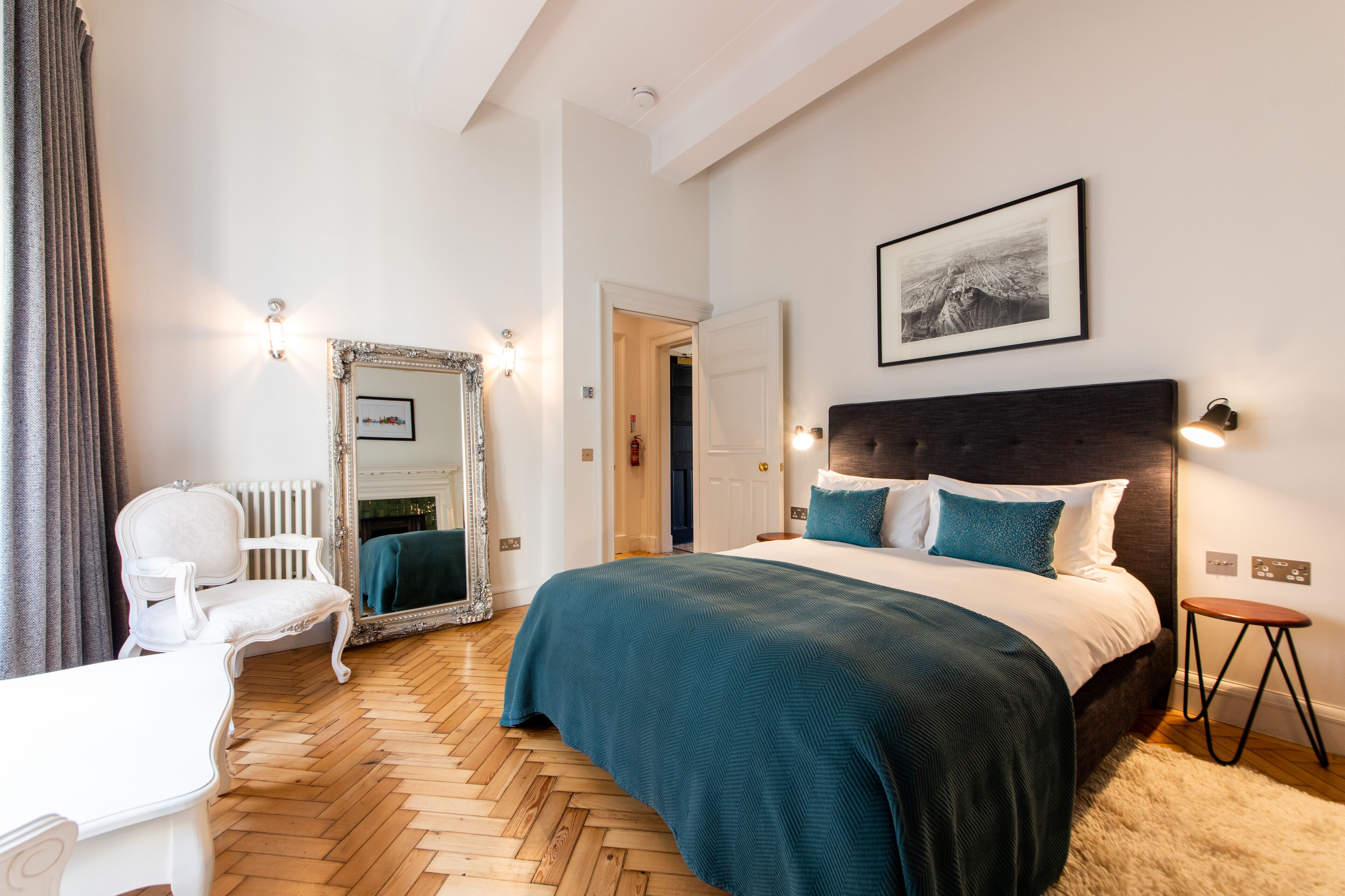 A bedroom with a large bed, a chair, a mirror, and a framed picture on the wall.