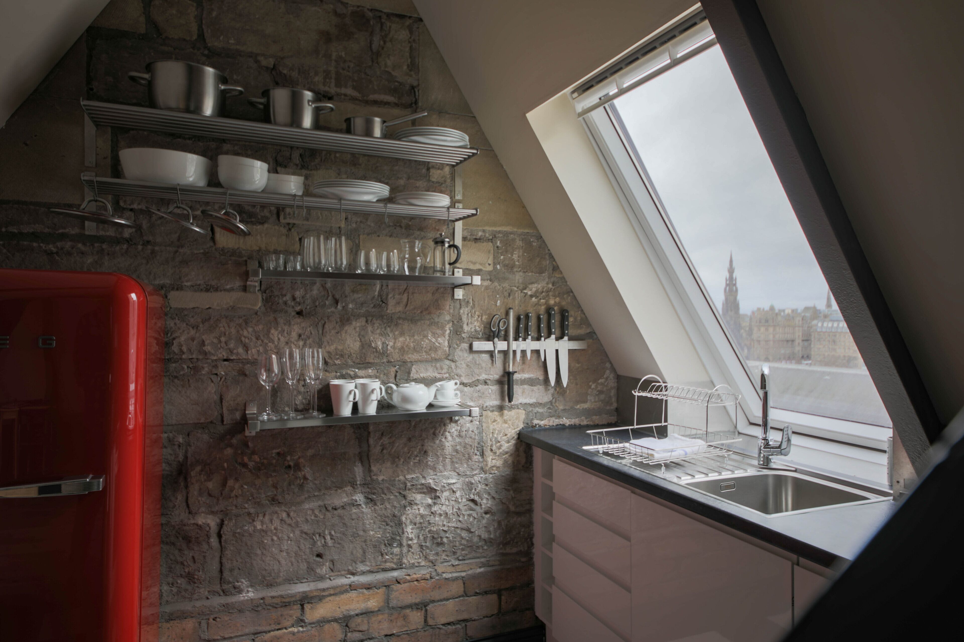 A kitchen with a stone wall, a red refrigerator, and a window with a view of a cityscape.