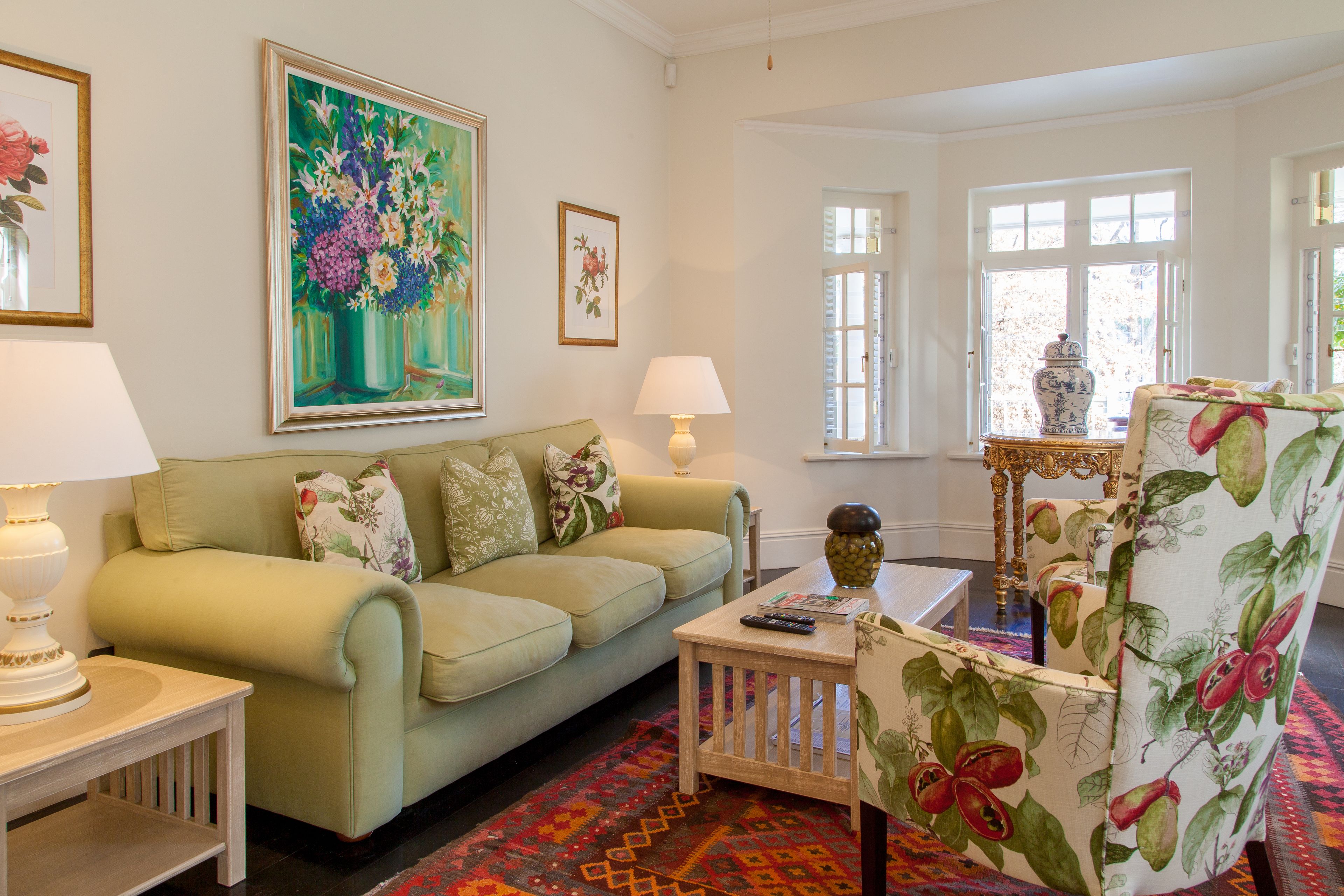 A living room with a green sofa, a patterned armchair, a small table with a lamp, and a colorful rug.
