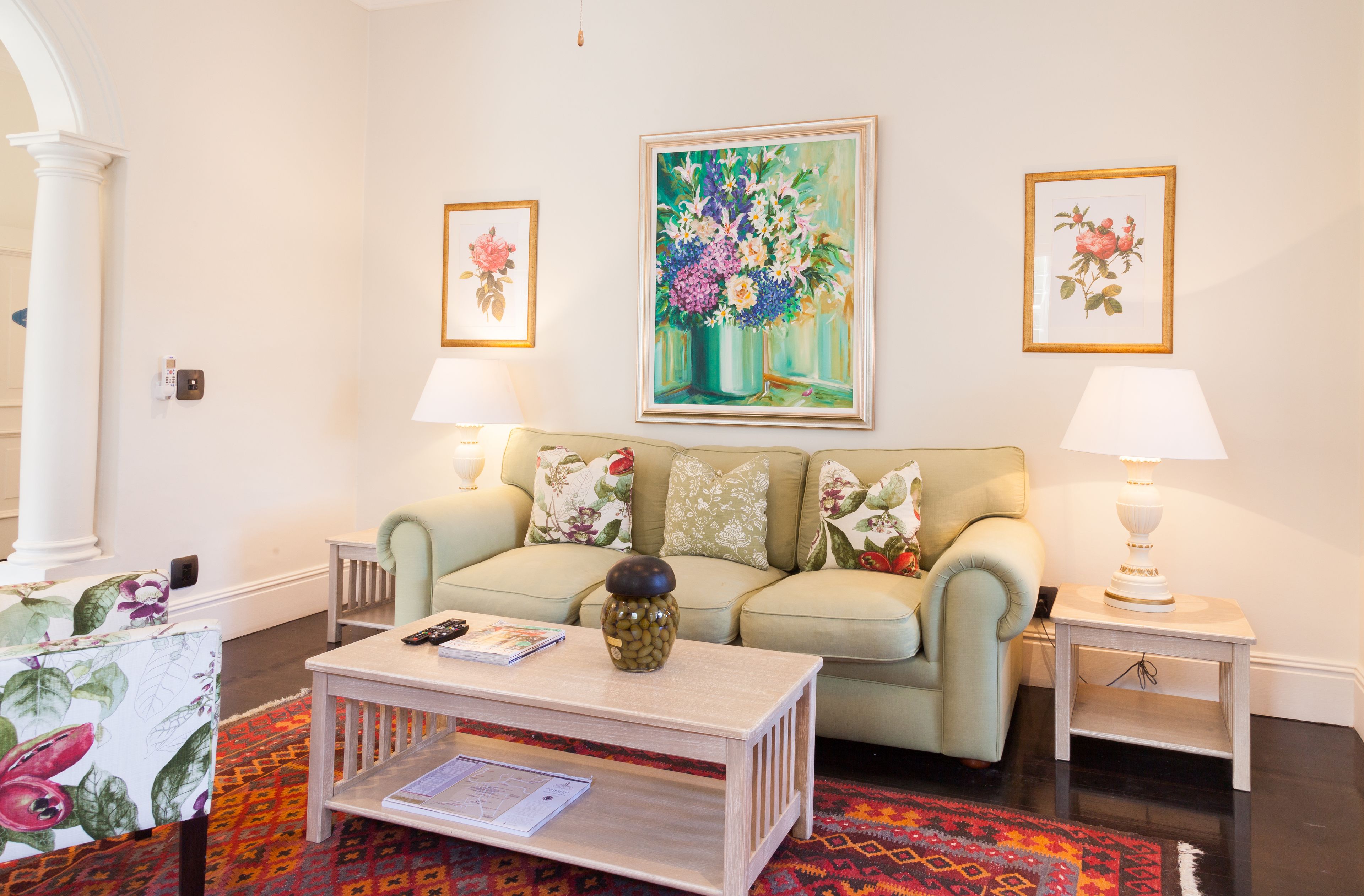 A living room with a sofa, a coffee table, and two lamps. There are floral paintings on the walls.