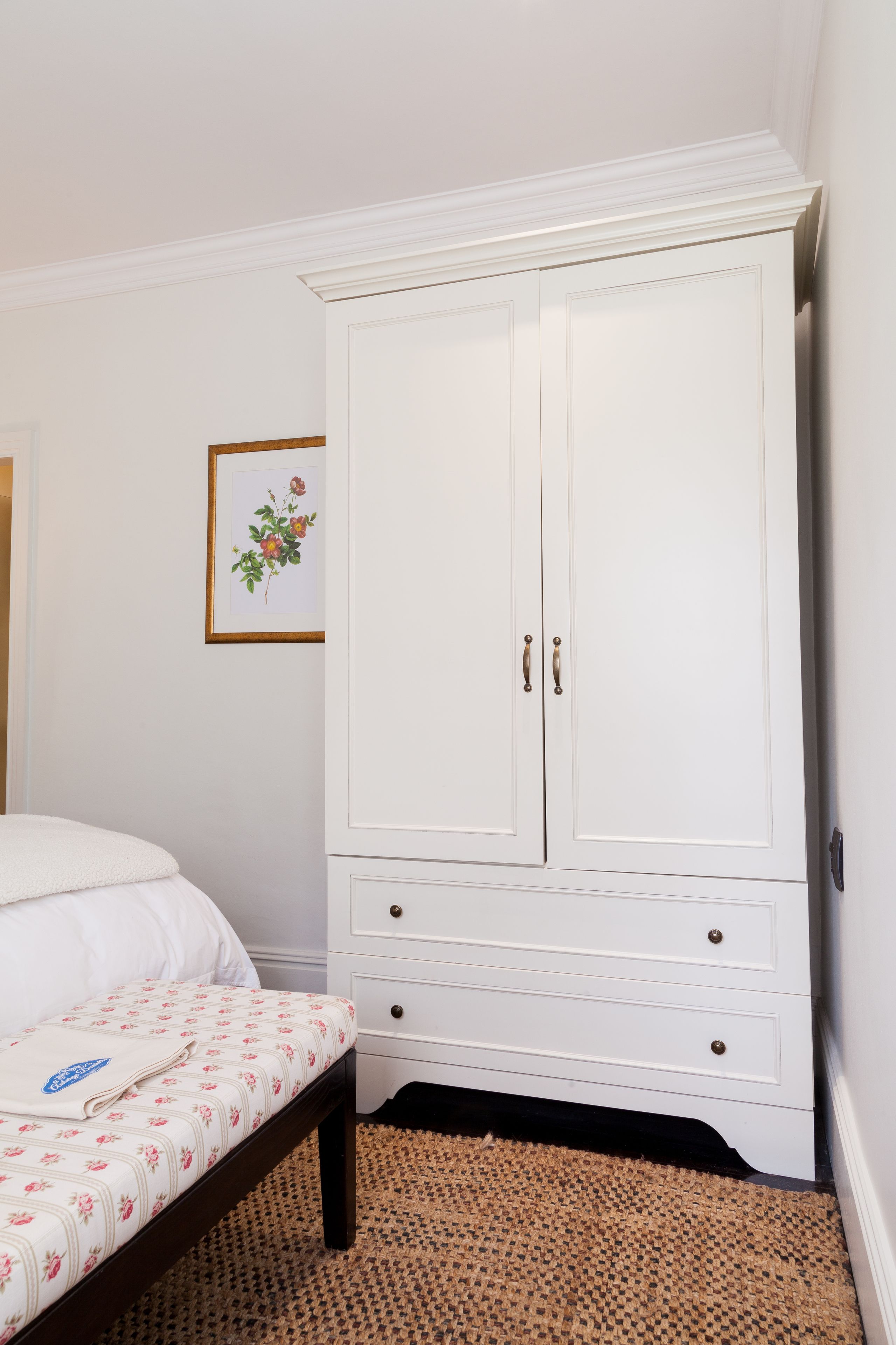Un dormitorio con una cama, un armario blanco y una obra de arte floral enmarcada en la pared.