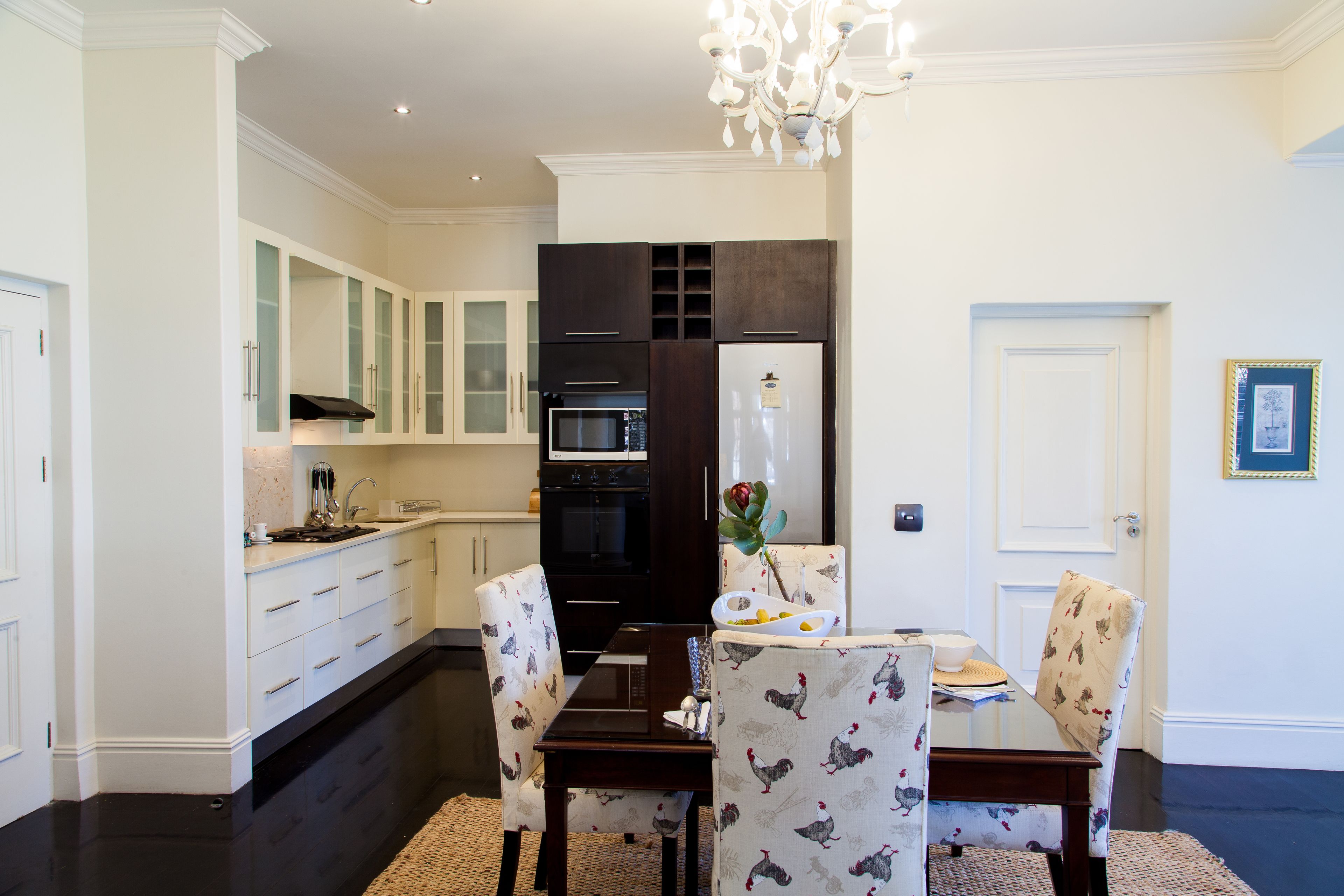 A modern kitchen with white cabinetry, a dark countertop, and a dining area with patterned chairs.
