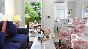 Een moderne woonkamer met een blauwe bank, een witte salontafel en een fauteuil met een patroon. Door een open deur is een eethoek met een tafel en stoelen te zien.