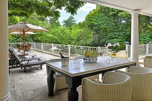 Une terrasse couverte avec une table dressée pour les repas, des chaises en osier et un grand parasol.
