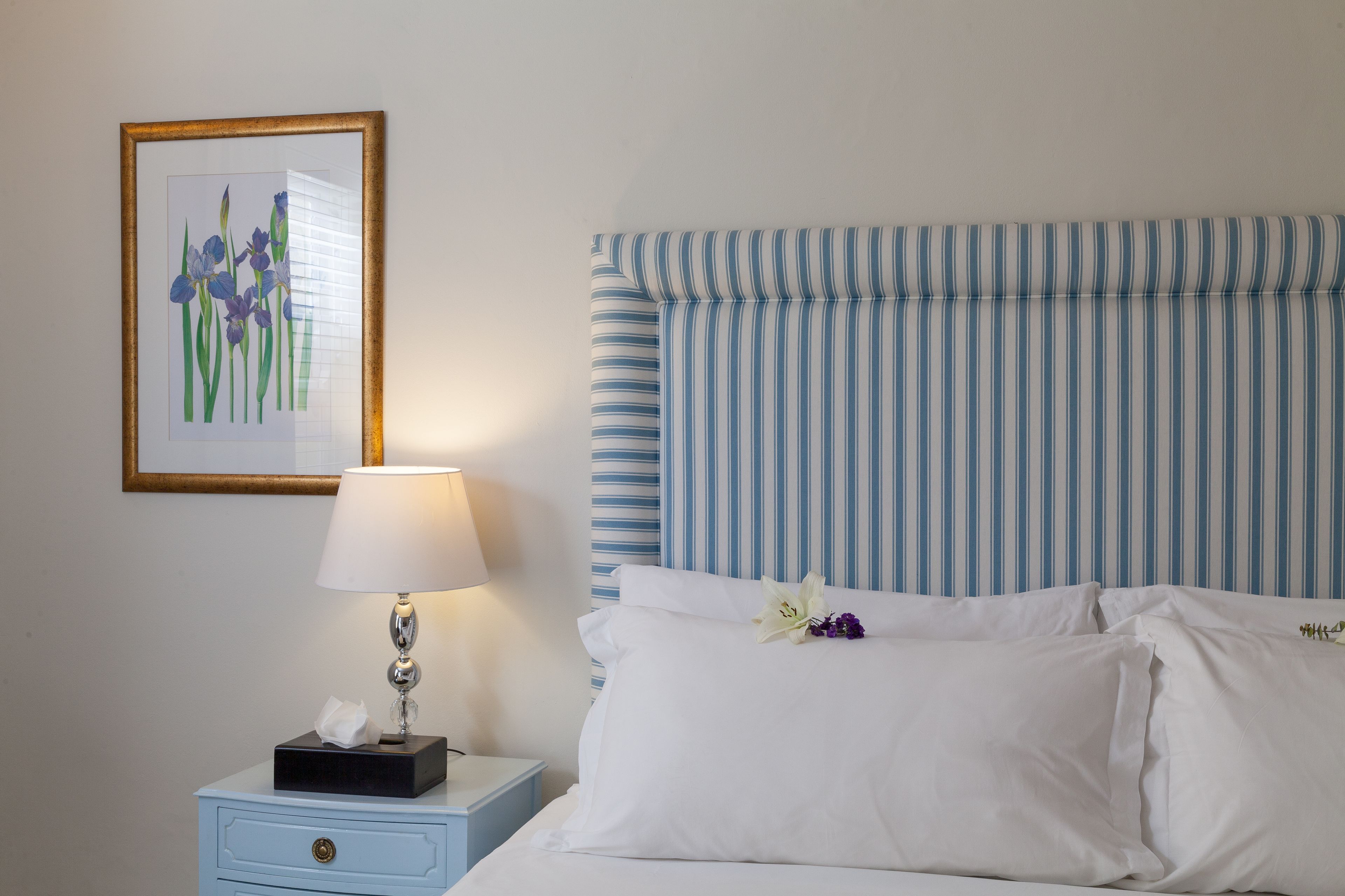 A neatly made bed with white linens, a striped headboard, and a bedside table with a lamp and a tissue box.