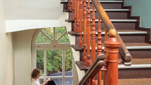 A staircase with wooden balusters and a person sitting on a landing reading a book. - EastSeven Berlin Hostel (Berlin)