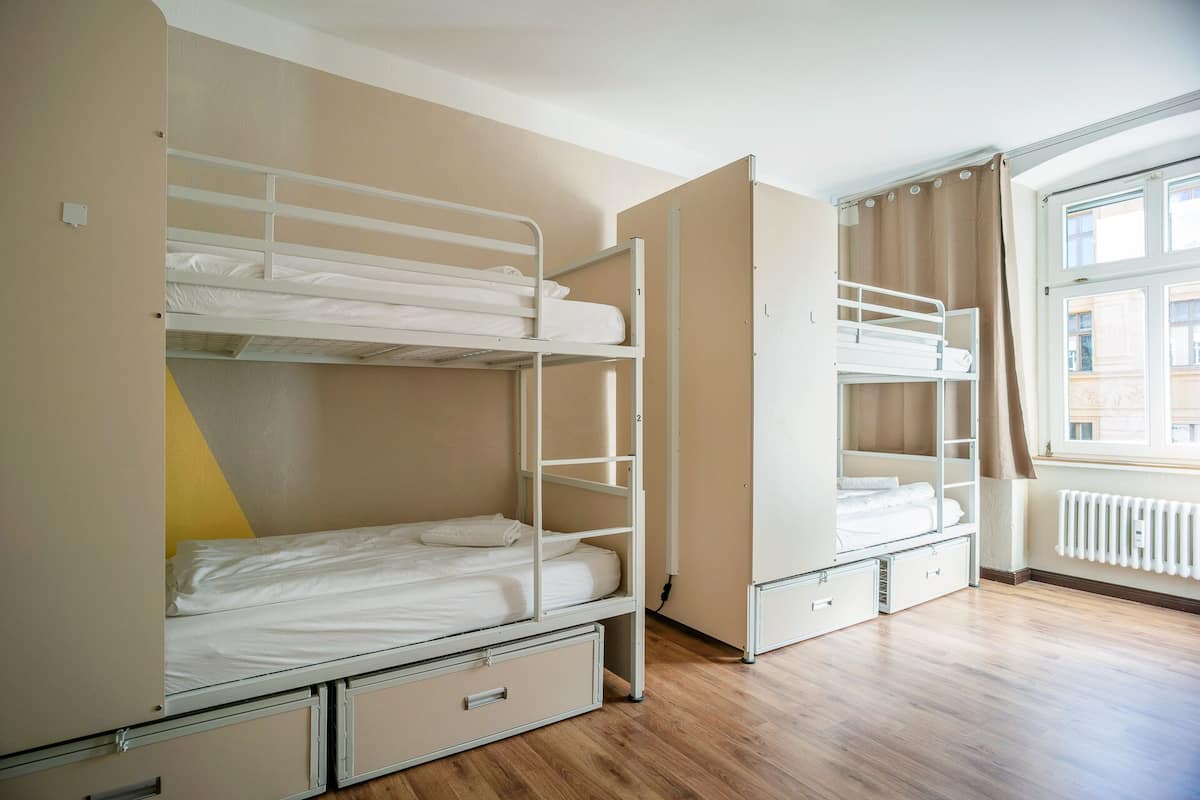 A dormitory room with bunk beds, a radiator, and a window with curtains.