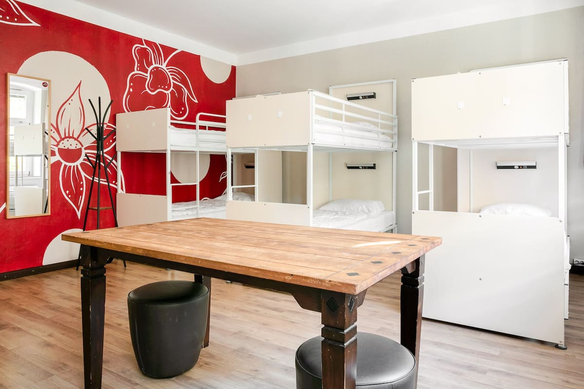 A room with bunk beds, a wooden table, and a red wall with a white design.