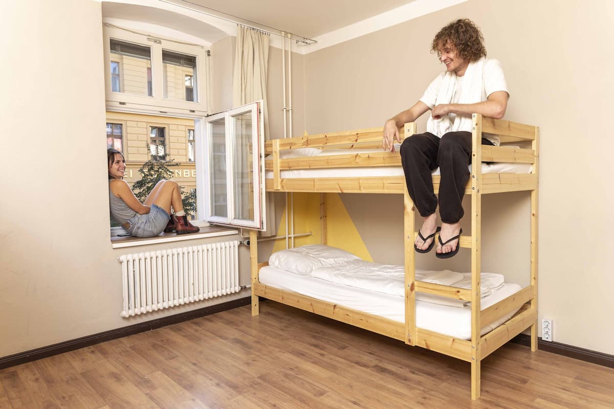 A bunk bed room with a window, a radiator, and a view of buildings outside.